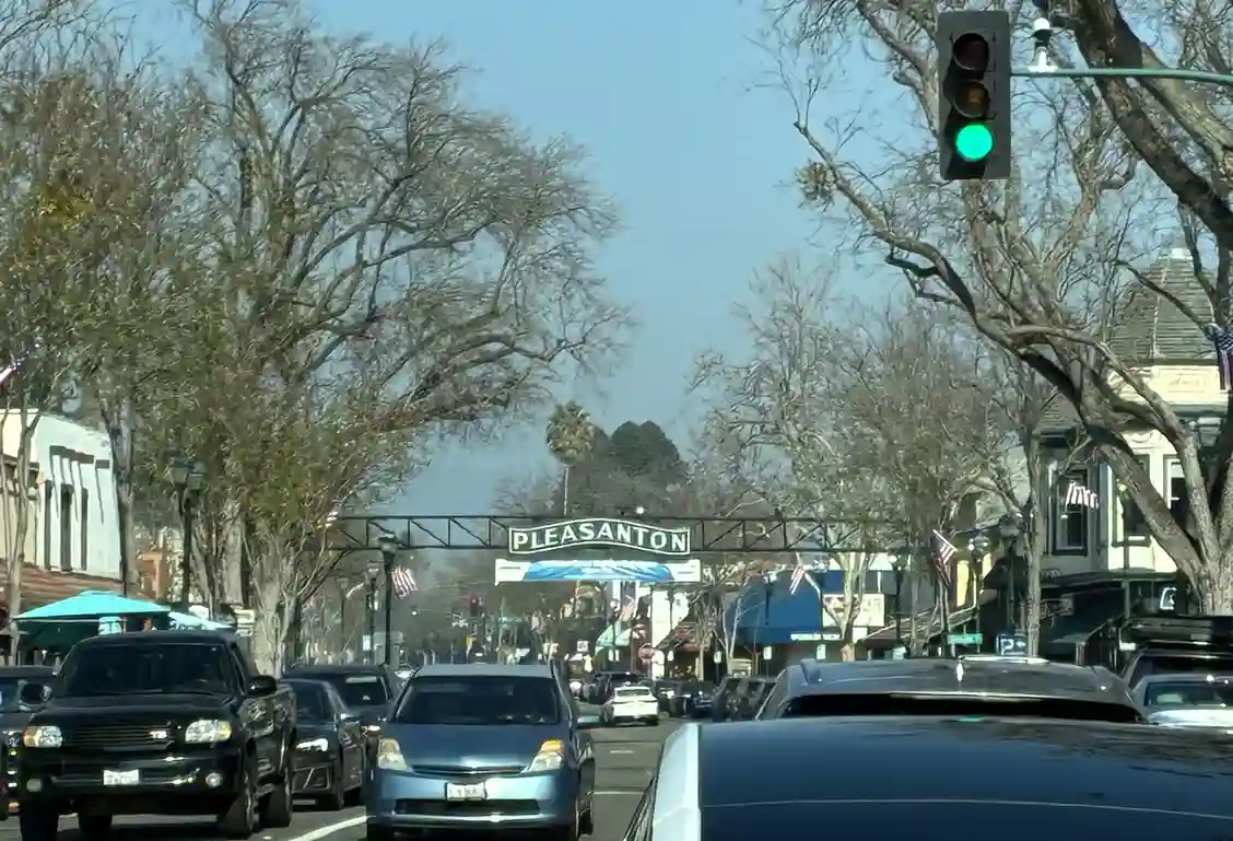 Pleasanton downtown street with green traffic light, parked cars, and historic buildings under bare trees